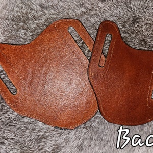 Puede incluir: Dos fundas de cuero marr&oacute;n con costuras en los bordes. Las fundas tienen dos recortes para los bucles del cintur&oacute;n. El texto "Back" est&aacute; escrito en blanco sobre fondo negro debajo de las fundas.