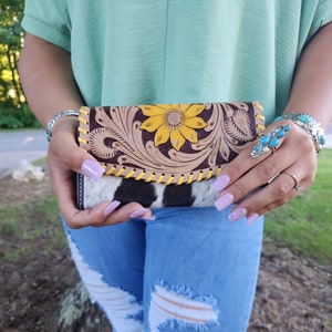 May include: A brown leather wallet with a floral design and a sunflower in the center. The wallet is made of cowhide and has a black and white pattern on the bottom half.