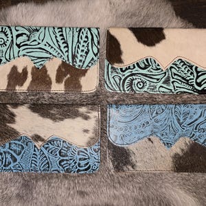 May include: Four leather wallets with a cowhide and embossed design. The wallets feature a combination of turquoise, light blue, and brown leather. The cowhide sections have a natural pattern.