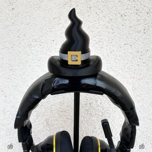 May include: Black headphone stand with a black witch hat on top. The hat has a gold buckle with the letter "B" on it.