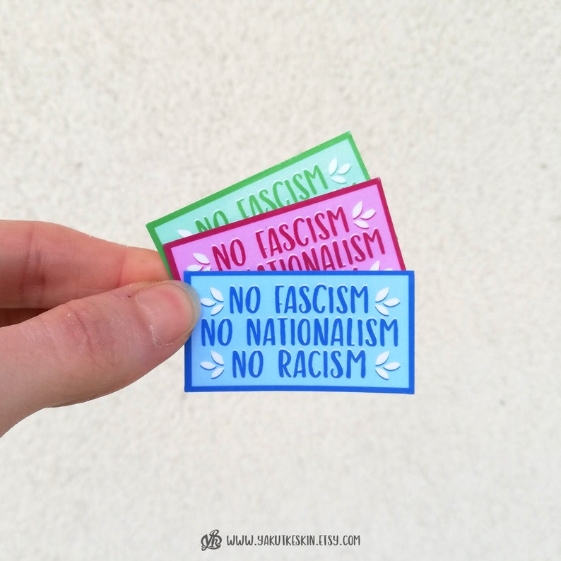 K&ouml;nnte beinhalten: Drei Aufkleber mit dem Text "No Fascism, No Nationalism, No Racism" in verschiedenen Farben: gr&uuml;n, rosa und blau. Jeder Aufkleber hat ein florales Design.