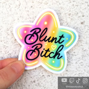 May include: A rainbow star-shaped sticker with the text "Blunt Bitch" in black lettering. The sticker has a neon glow effect around the edges.