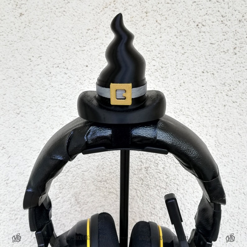 May include: Black headphone stand with a black witch hat on top. The hat has a gold buckle with the letter "B" on it.