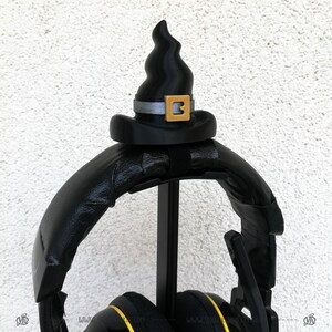 May include: Black headphones with a black witch hat on top. The hat has a gold buckle with the number 3 on it.