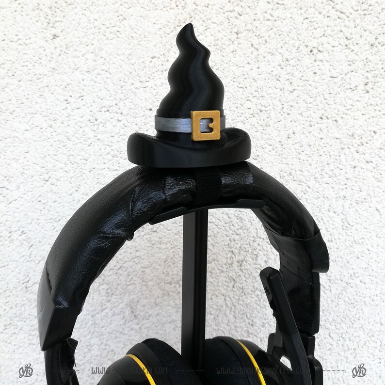 May include: Black headphones with a black witch hat on top. The hat has a gold buckle with the number 3 on it.