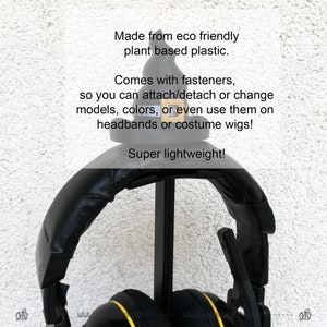 May include: Black headphones with yellow accents are hanging on a black stand. The headphones are made from eco-friendly plant-based plastic and come with fasteners to attach or detach them. The text "Super lightweight!" is visible in the image.