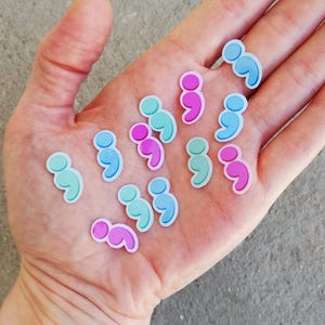 May include: A hand holding a variety of colorful semicolon stickers. The stickers are in shades of blue, pink, and green.