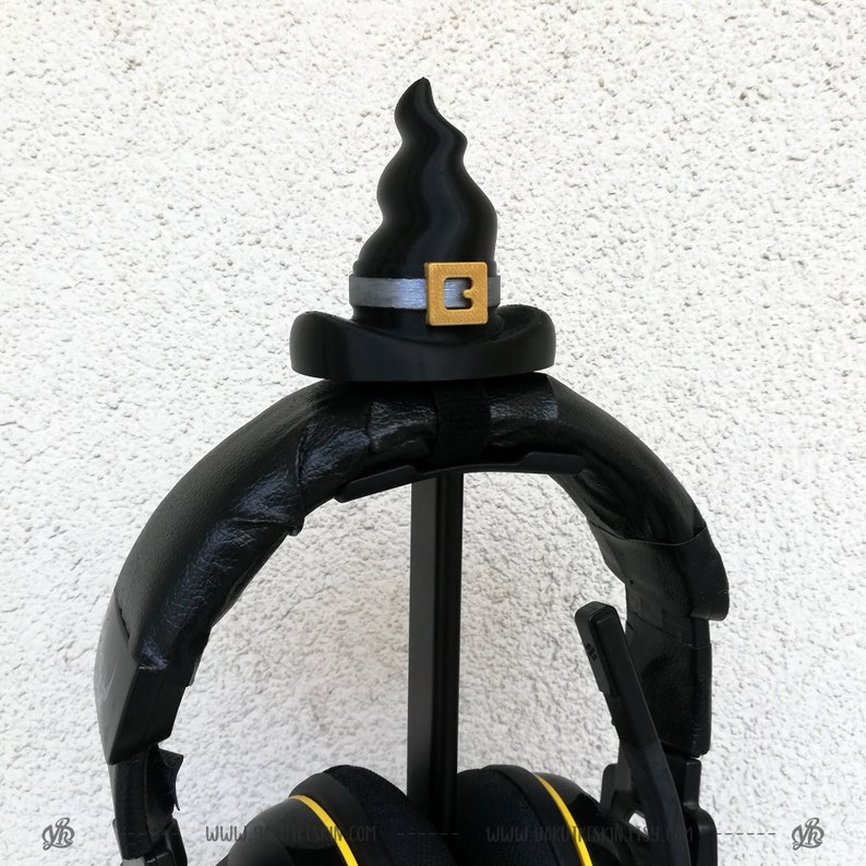 May include: Black headphones with a black witch hat on top. The hat has a gold buckle with the number "3" on it.