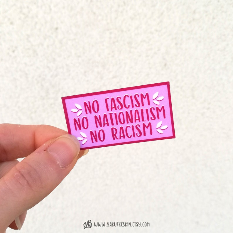 K&ouml;nnte beinhalten: Rosafarbener Aufkleber mit dem Text "NO FASCISM NO NATIONALISM NO RACISM" in roten Buchstaben mit wei&szlig;en floralen Akzenten.