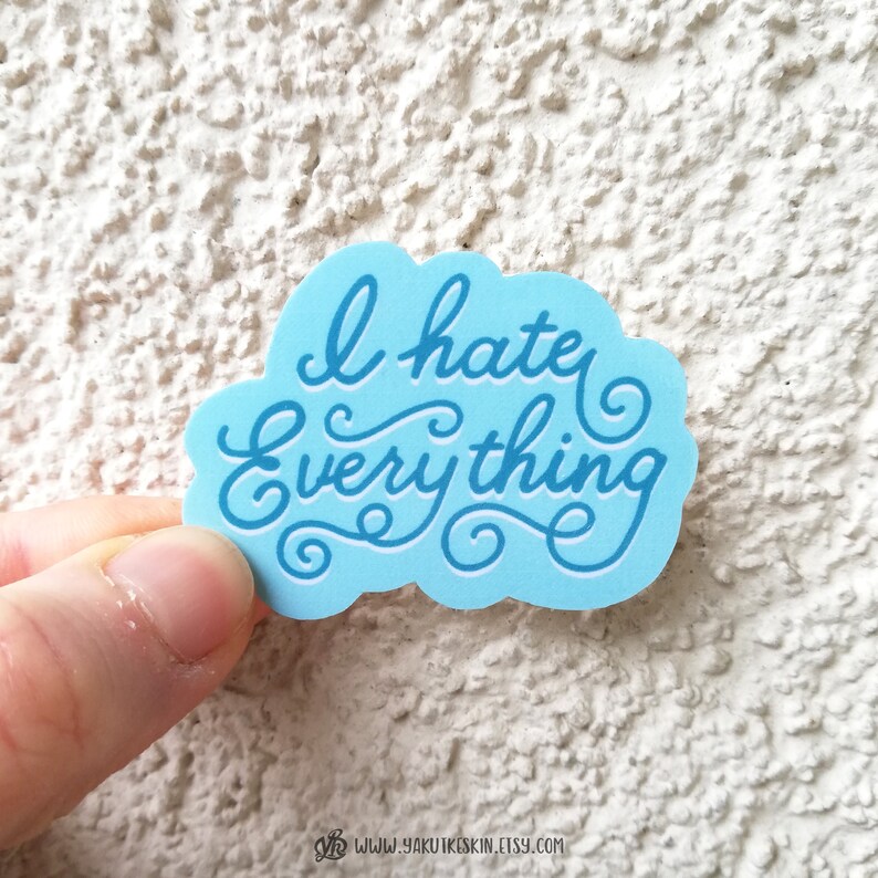 May include: A blue sticker with white lettering that says "I hate everything" in a cursive font.