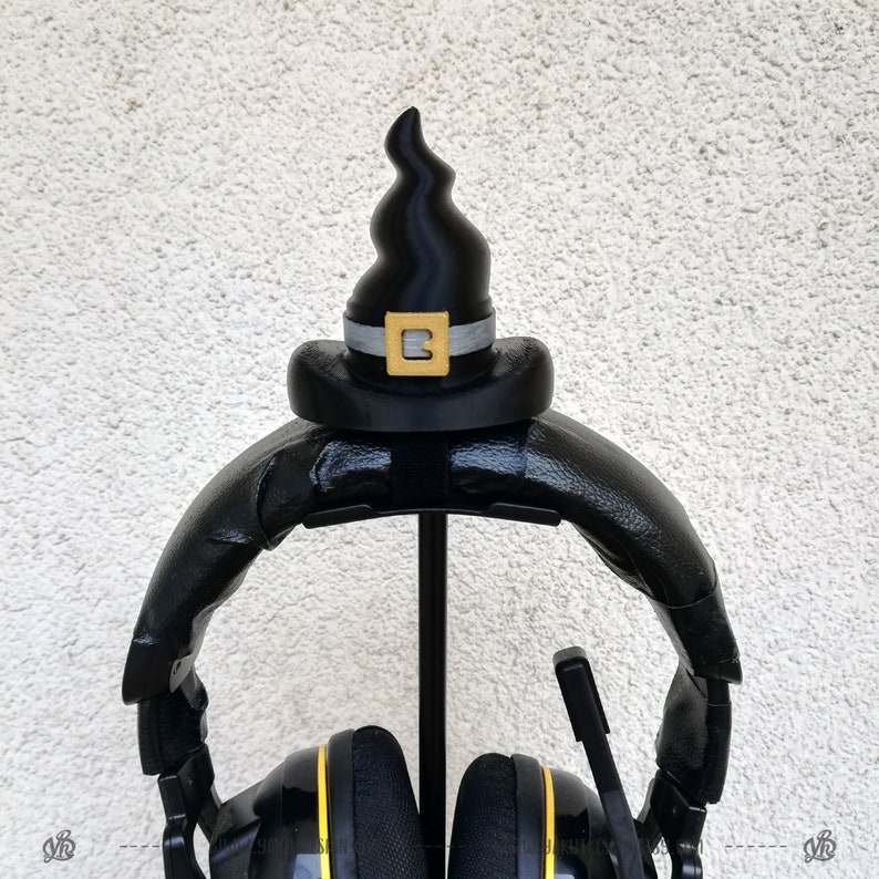 May include: Black headphones with a black witch hat on the stand. The hat has a silver band and a gold letter "B" on the front.