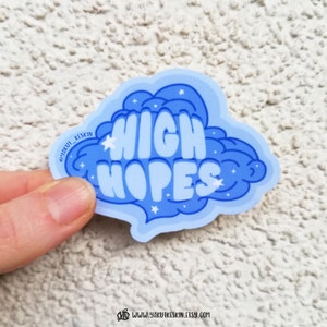 Puede incluir: Pegatina azul y blanca en forma de nube con el texto "HIGH HOPES". La pegatina tiene un dise&ntilde;o brillante.