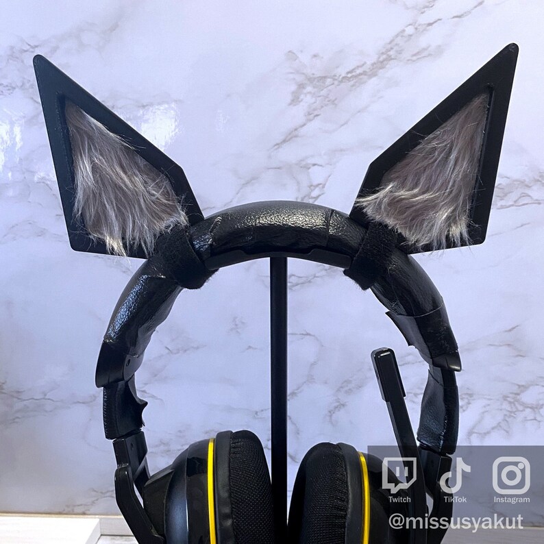 May include: Black gaming headset with faux fur wolf ears attached to the headband. The headset has yellow accents on the earcups and a microphone.