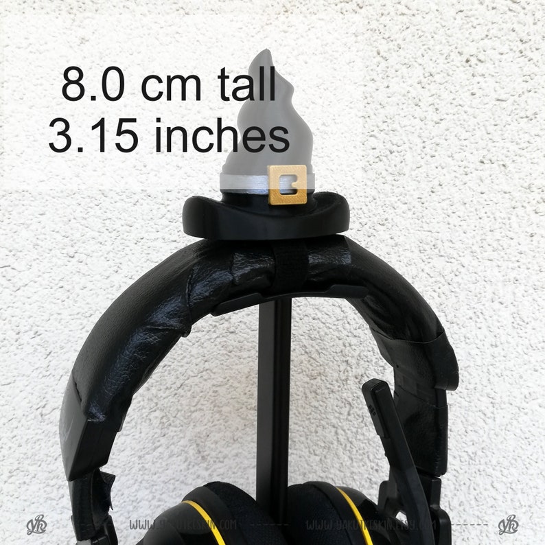 May include: Black headphones with a black and silver witch hat on top of the stand. The hat is 8.0 cm tall or 3.15 inches tall.