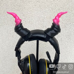 May include: Black headphones with a yellow accent on the earcups. The headphones have pink devil horns attached to the headband.