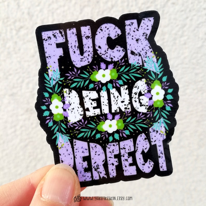 K&ouml;nnte beinhalten: Ein schwarzer und wei&szlig;er Aufkleber mit lila Schriftzug, der "F**k Being Perfect" lautet, umgeben von einem floralen Design mit gr&uuml;nen Bl&auml;ttern und wei&szlig;en Bl&uuml;ten.