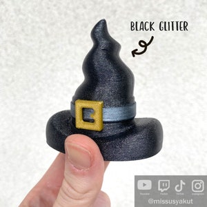 May include: Black glitter witch hat with a gold buckle and a silver band. The hat is 3D printed and has a pointed top.