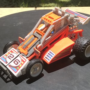 Könnte beinhalten: Orangefarbenes und weißes Spielzeug-Rennwagen mit der Nummer 26 an der Seite. Das Auto hat einen grauen Überrollkäfig und einen weißen Spoiler.