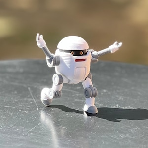 以下が含まれることがあります： グレーのアクセントと赤い目をした白いロボットのおもちゃが、グレーの表面に腕を伸ばして立っています。
