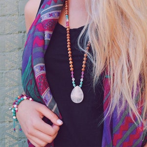 May include: A woman wearing a colorful patterned scarf and a black tank top with a long, beaded necklace featuring a large, teardrop-shaped, light pink gemstone pendant.