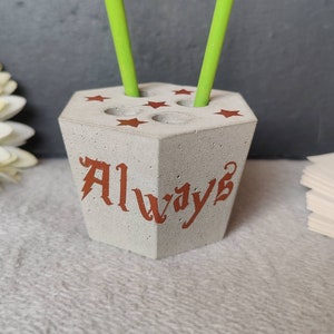 Könnte beinhalten: Ein grauer Betonstifthalter mit fünf Fächern und dem Wort "Always" in brauner Schrift. Der Halter hat fünf rote Sterne um die Oberseite.