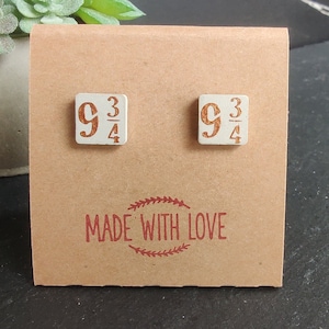 Op de afbeelding: Een paar witte keramische oorbellen met de breuk 9 3/4 gedrukt in oranje op elke oorbel. De oorbellen worden getoond op een bruine kaart met de woorden "MADE WITH LOVE" gedrukt in rood.