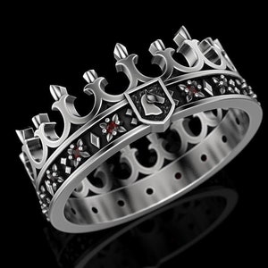 Puede incluir: Un anillo de plata con un diseño de corona y piedras preciosas rojas. La corona presenta un escudo con una cabeza de caballo.