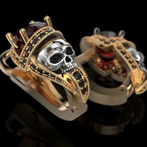 May include: A pair of gold earrings featuring a skull design and a red gemstone. The earrings are adorned with black gemstones.