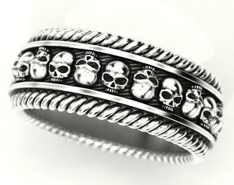 May include: A silver ring featuring a rope-like design and a row of skull engravings.