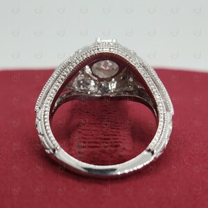 May include: A silver engagement ring with a large, round, clear center stone and smaller, clear stones surrounding it. The ring has a detailed, ornate design.