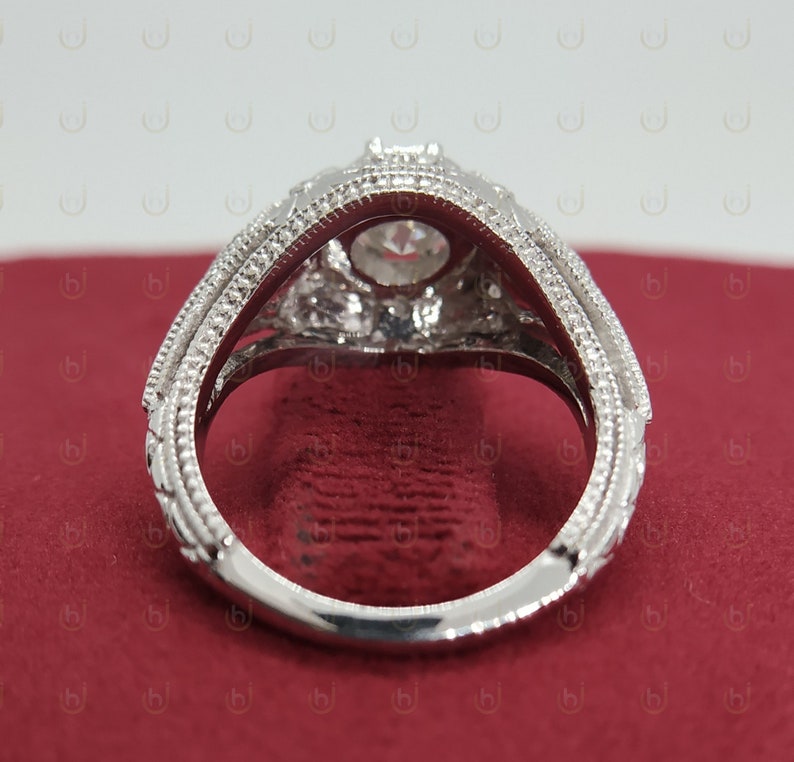 May include: A silver engagement ring with a large, round, clear center stone and smaller, clear stones surrounding it. The ring has a detailed, ornate design.