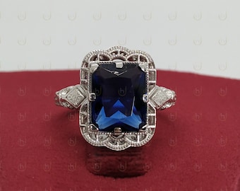 May include: A silver ring with a large, dark blue, emerald-cut gemstone set in a filigree design.