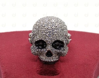 Könnte beinhalten: Ein silberner Totenkopfring mit schwarzen Augenhöhlen und einem mit weißen Diamanten besetzten Design.