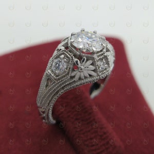 May include: A silver ring with a large, round, clear gemstone surrounded by smaller gemstones and intricate floral designs.