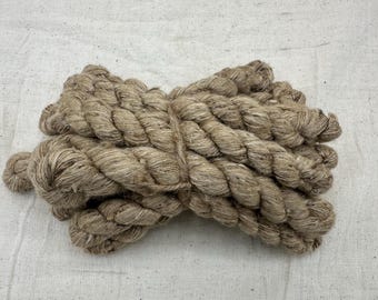 May include: A close-up of a bundle of natural fiber rope, likely jute or hemp, in a light brown color. The rope is twisted and knotted, creating a textured and rustic appearance.