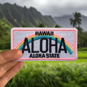 May include: White patch with a pink border featuring a rainbow and the text "HAWAII ALOHA ALOHA STATE" in black.