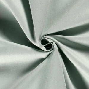 May include: A solid light sage green fabric with a visible woven texture. The material is gathered in the centre, creating deep, radiating folds and shadows that highlight the smooth, matte surface and the consistent colour throughout the textile.