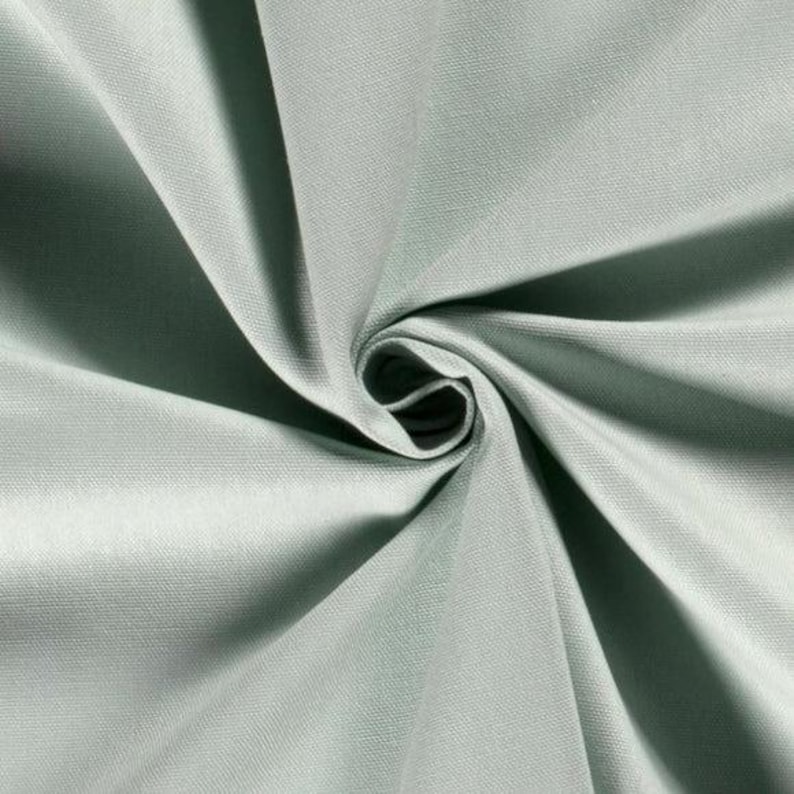 May include: A solid light sage green fabric with a visible woven texture. The material is gathered in the centre, creating deep, radiating folds and shadows that highlight the smooth, matte surface and the consistent colour throughout the textile.