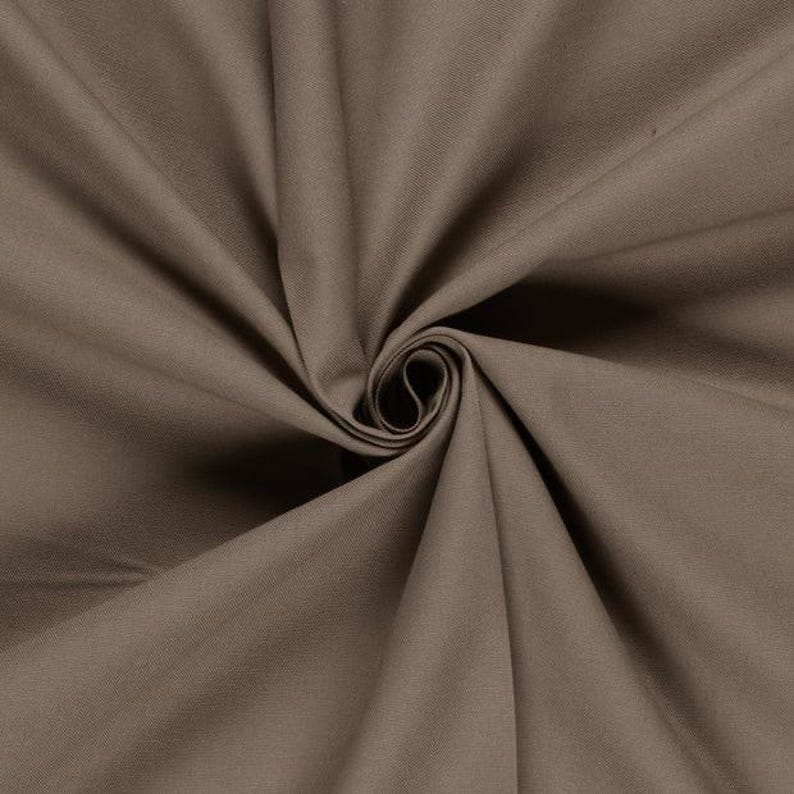May include: A solid taupe-coloured fabric featuring a dense, woven texture. The material is gathered in the centre, creating deep, radiating folds and shadows that highlight the smooth, matte surface and the consistent earthy brown tone throughout.