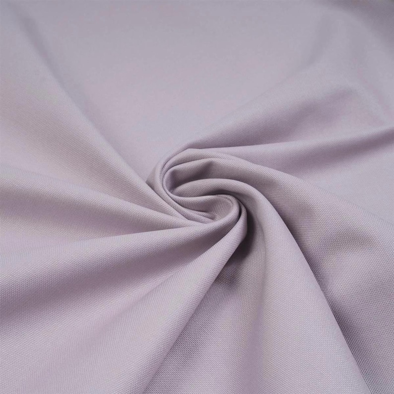 May include: A solid light lavender fabric with a smooth, matte texture. The material is gathered in the centre, creating soft, radiating folds and drapes that highlight the consistent, uniform colour and fine weave of the textile surface.
