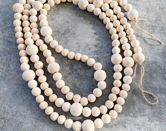 May include: A set of four wooden bead garlands in a natural beige color. The garlands are made of round wooden beads of varying sizes and are strung together with twine.