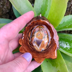 Op de afbeelding: Een bruine houten hanger met een transparante harsinleg met een kleurrijke agaat steen. De hanger heeft een zilveren lus om op te hangen.
