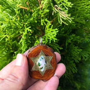 May include: A wooden pendant with a gold-toned six-pointed star design and a green and white gemstone in the center.