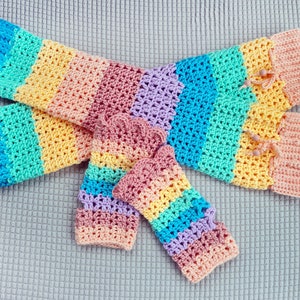 Könnte beinhalten: Ein Paar regenbogenfarbene gestrickte Armwärmer mit einem passenden Paar Fingerhandschuhen. Die Armwärmer haben ein Farbschema in Pink, Gelb, Blau und Grün. Die Handschuhe haben ein ähnliches Farbschema, sind aber etwas dezenter.