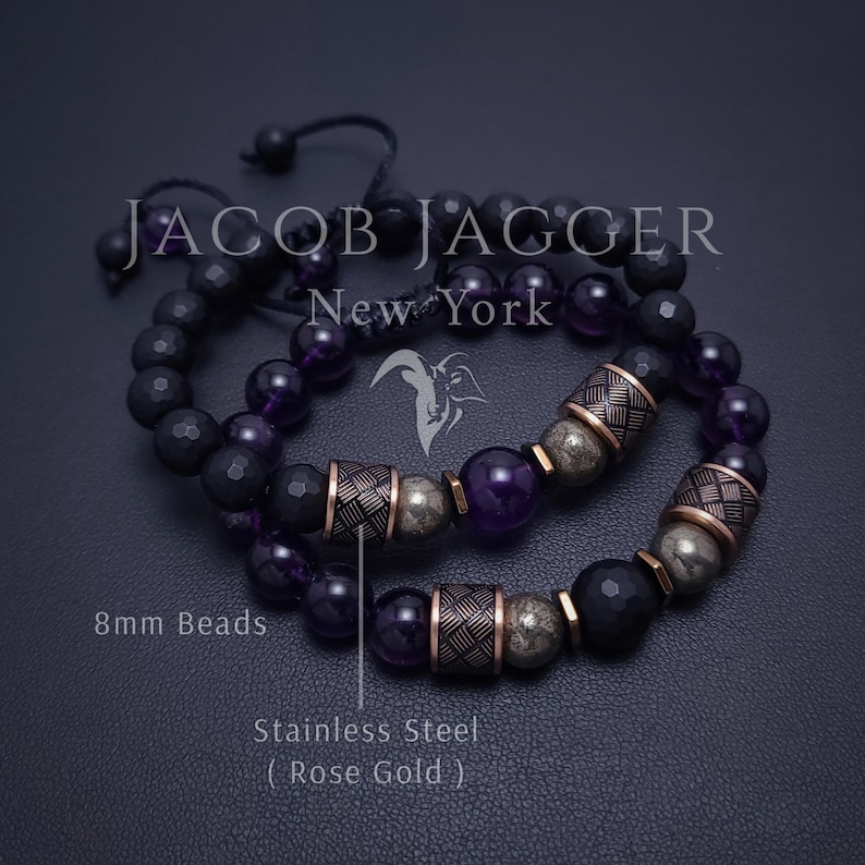 May include: Two bracelets with 8mm beads. One bracelet has black beads and the other has amethyst beads. Both bracelets have rose gold stainless steel spacers and pyrite beads. The bracelets are on a black surface. The text "JACOB JAGGER New York" is visible in the image.