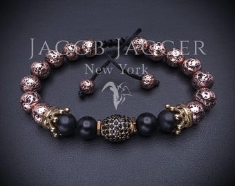 Op de afbeelding: Een kralenarmband met roze goudkleurige, getextureerde lavakralen, gladde zwarte bolvormige kralen en een centrale kraal ingelegd met kleine zwarte kristallen. Twee goudkleurige, kroonvormige tussenstukken flankeren het midden van de armband.