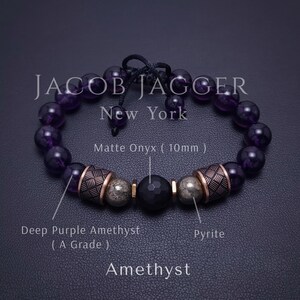 May include: A purple amethyst gemstone bracelet with a matte onyx bead, pyrite beads, and gold-toned metal accents. The bracelet is made by JACOB JAGGER New York.
