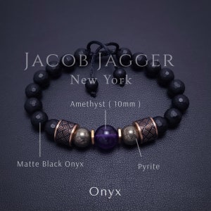 May include: Black onyx gemstone bracelet with gold accents and a purple amethyst gemstone. The bracelet is made by Jacob Jagger New York.
