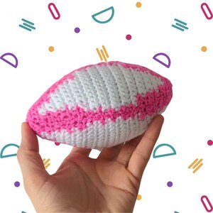 May include: A pink and white crocheted football shaped toy. The toy is made with white yarn and has pink stripes.