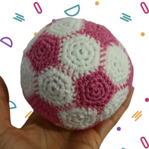 May include: A crocheted soccer ball with pink and white panels. The ball is made with a textured yarn and has a slightly bumpy surface.